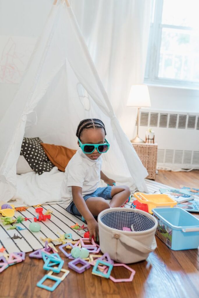 A child wearing sunglasses enjoys playtime in a cozy teepee surrounded by colorful toys.