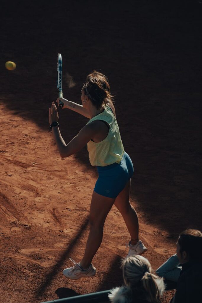 A woman hitting a tennis ball with a racket during a match on a clay court, showcasing athletic skill.