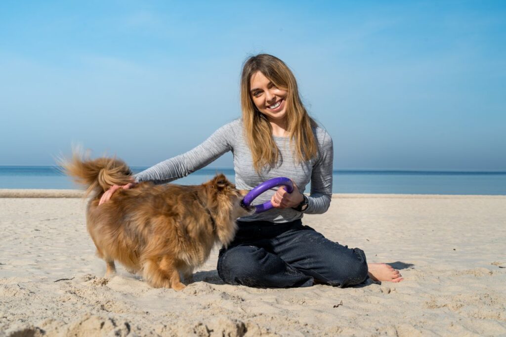 A joyful woman playing with her fluffy dog on the sandy beach of Kołobrzeg, Poland.