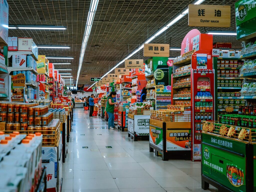 A vibrant supermarket aisle filled with diverse products and shoppers under bright lighting.